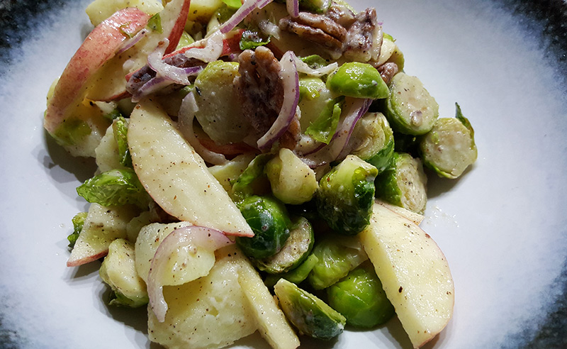 Aardappelsalade met geroosterde spruitjes, appel, geroosterde peccannoten en honing-mosterddressing